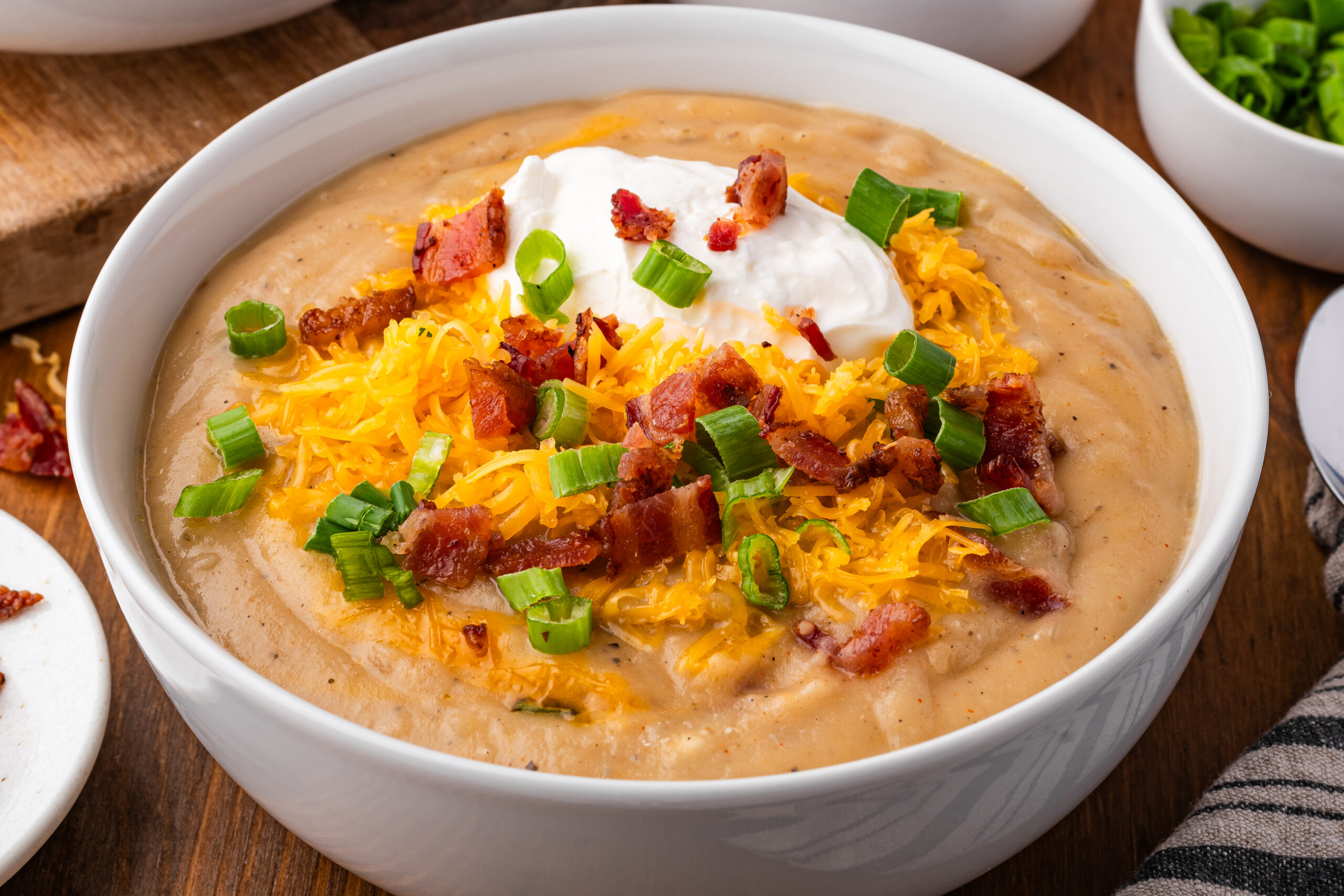up close shot of the Crock pot loaded baked potato soup in a white bowl topped with bacon, cheese and sour cream