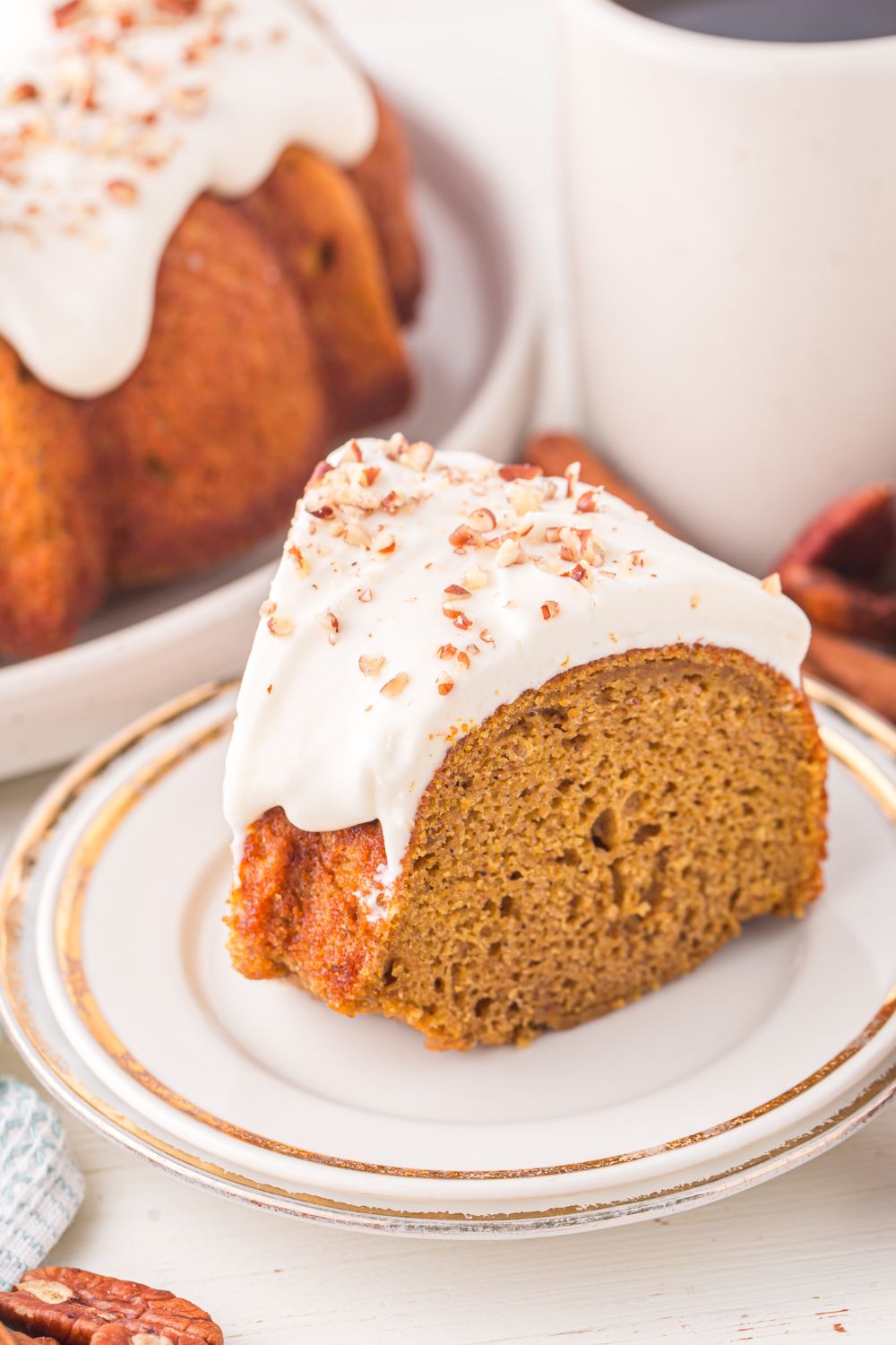 slice of Pumpkin Bundt Cake on a plate on the table with a glass of milk behind it and the rest of the cake to side 
