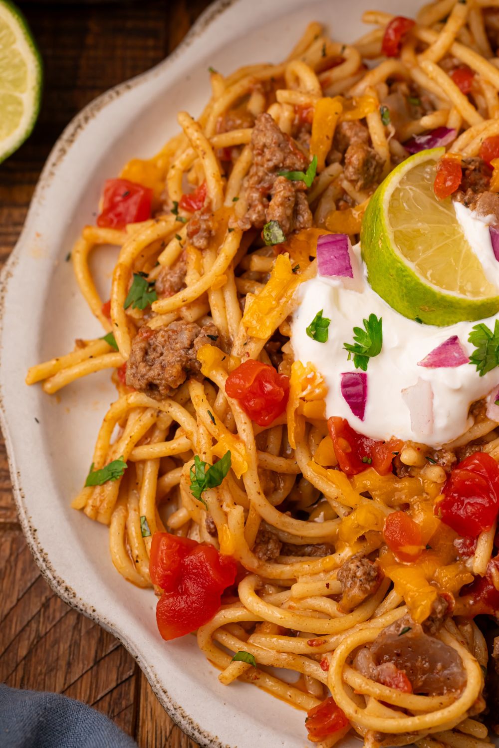 view of half a plate on wooden table with a full plate of Cheesy Taco Spaghetti on it 