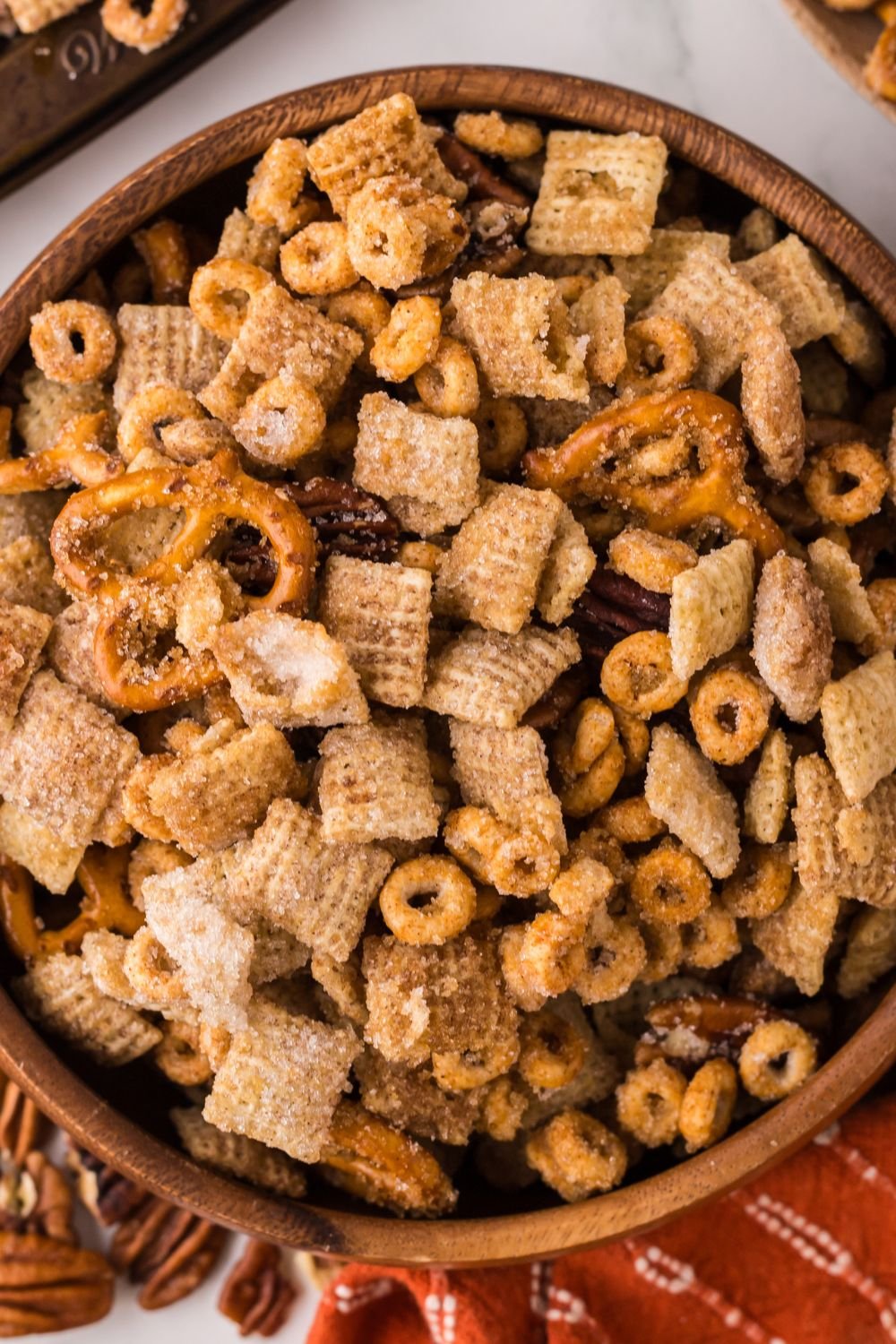 Pumpkin Spice Chex Mix in a wooden bowl and more around table and a towel under the bowl 