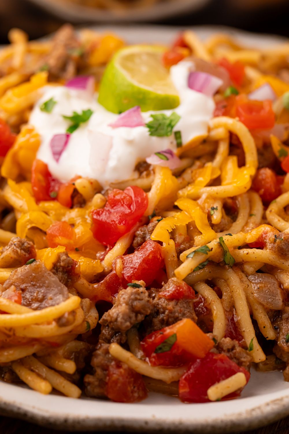 Taco spaghetti skillet on a white plate with a dollop of sour cream in center, cilantro, and a lime wedge