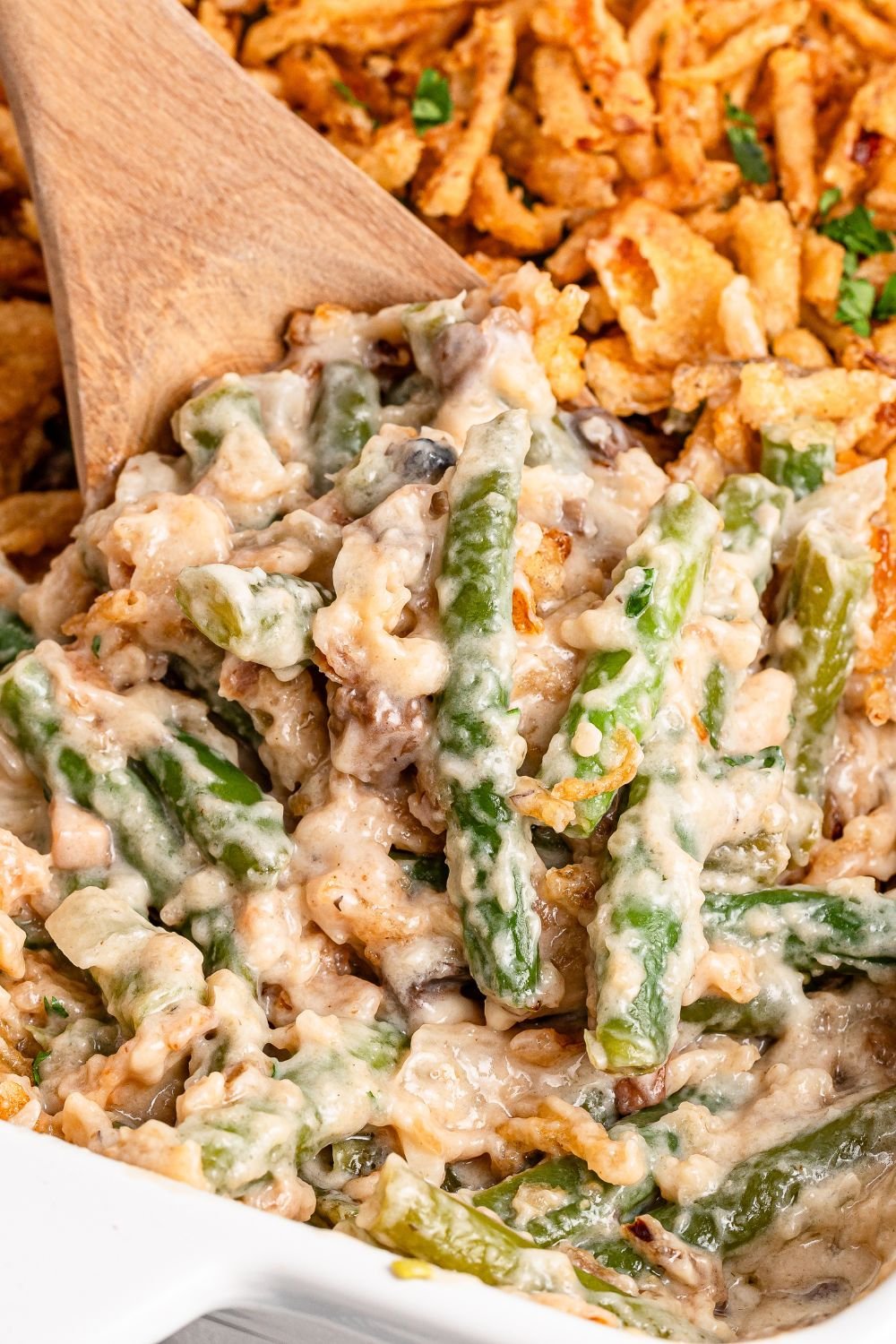 wooden spoon scooping up some of the Green Bean Casserole in a white baking dish on table 