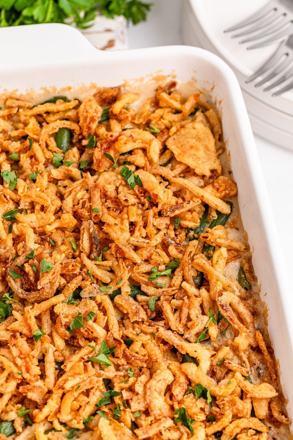Green Bean Casserole in a white pan on table with plates and fork to side 