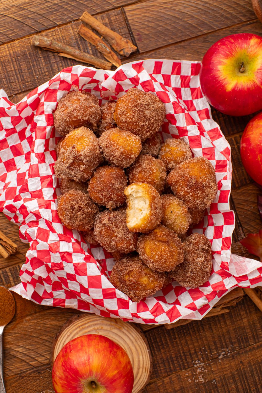 looking down at a wooden table with apples, cinnamon sticks and basket full of Apple Pie Donut Holes in the center