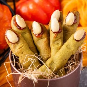 Witch Finger Cookies in a basket with straw in it with pumpkins and leaves on the table behind it