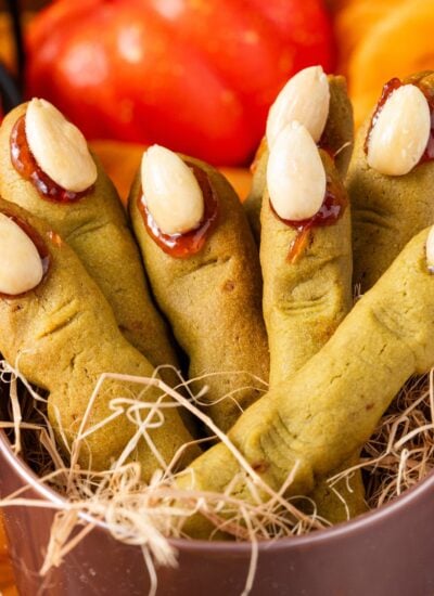 Witch Finger Cookies in a basket with straw in it with pumpkins and leaves on the table behind it