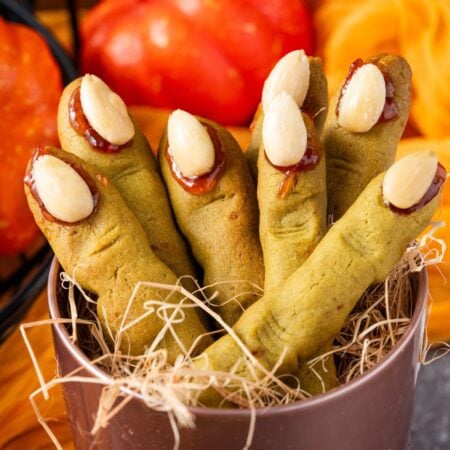 Witch Finger Cookies in a basket with straw in it with pumpkins and leaves on the table behind it
