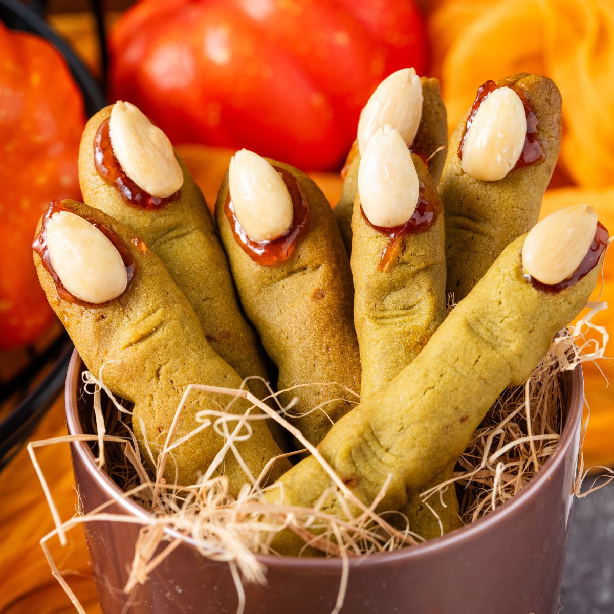 Witch Finger Cookies in a basket with straw in it with pumpkins and leaves on the table behind it 