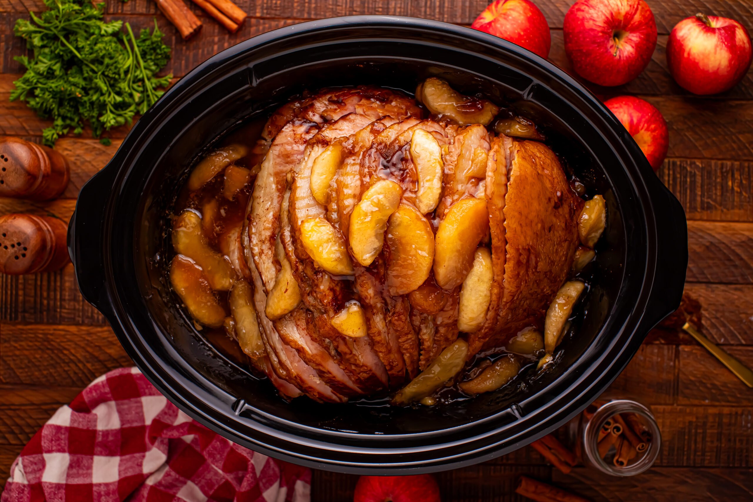 Slow Cooker Apple Glazed Ham in a black crock pot on a dark wood table 