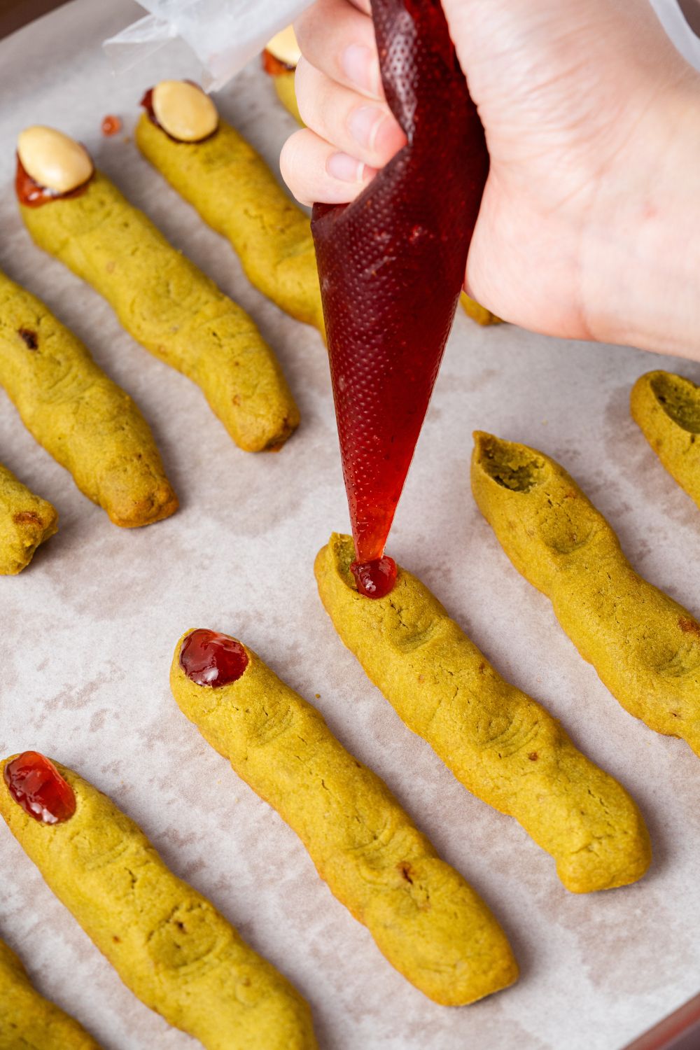 piping some jam on the tip of each of the Witch Finger Cookies on the baking tray 