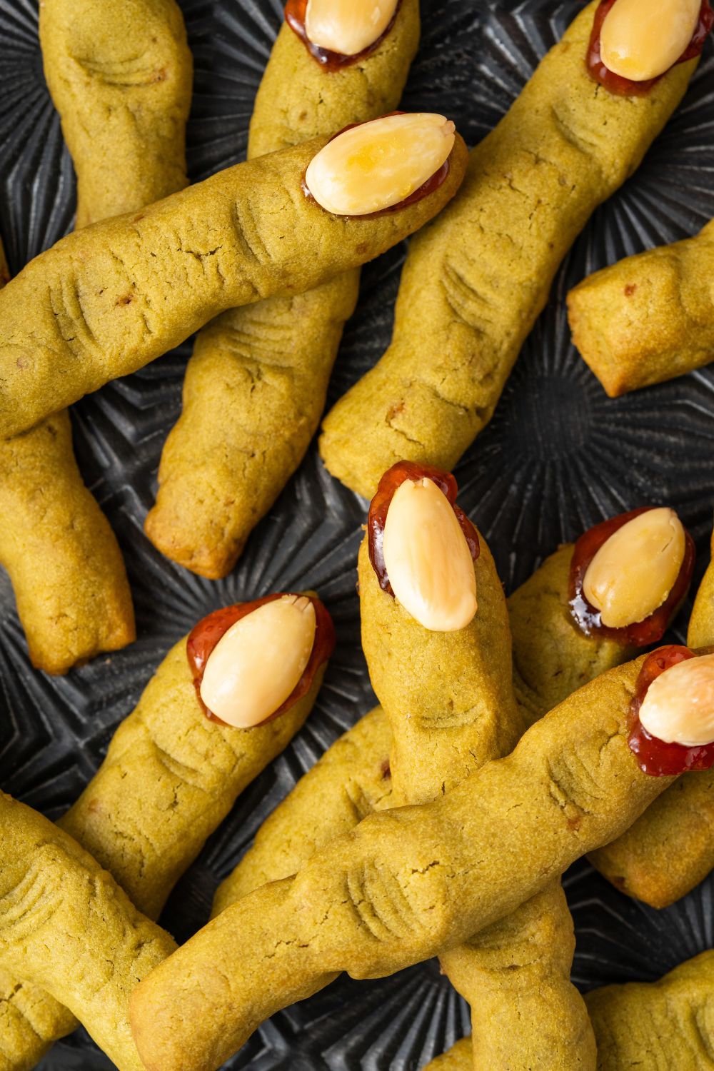 Witch Finger Cookies on a black tray. The cookies are scattered around the tray