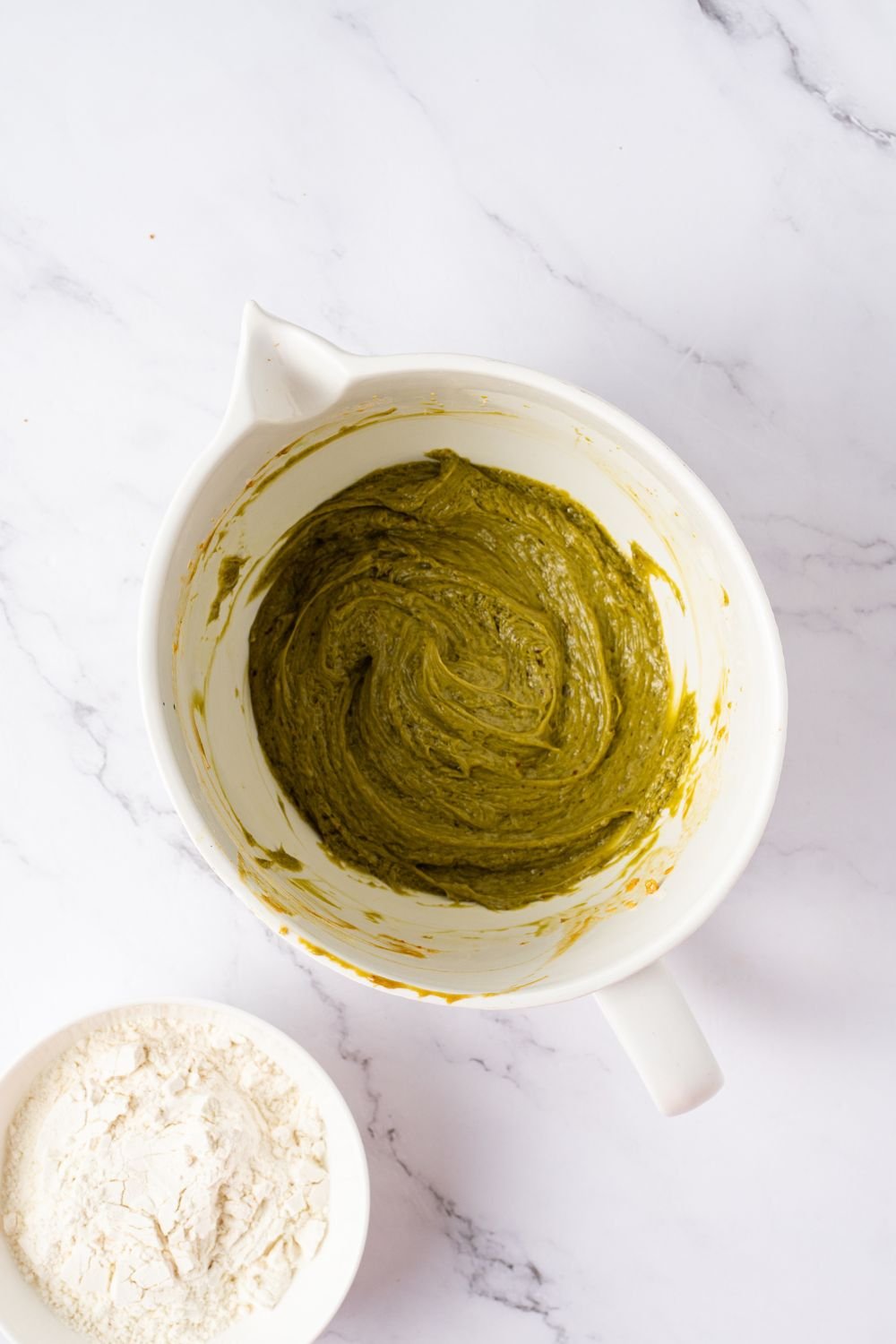 green pistachio cookie dough in a white bowl on table with pistachio butter and vanilla to side 
