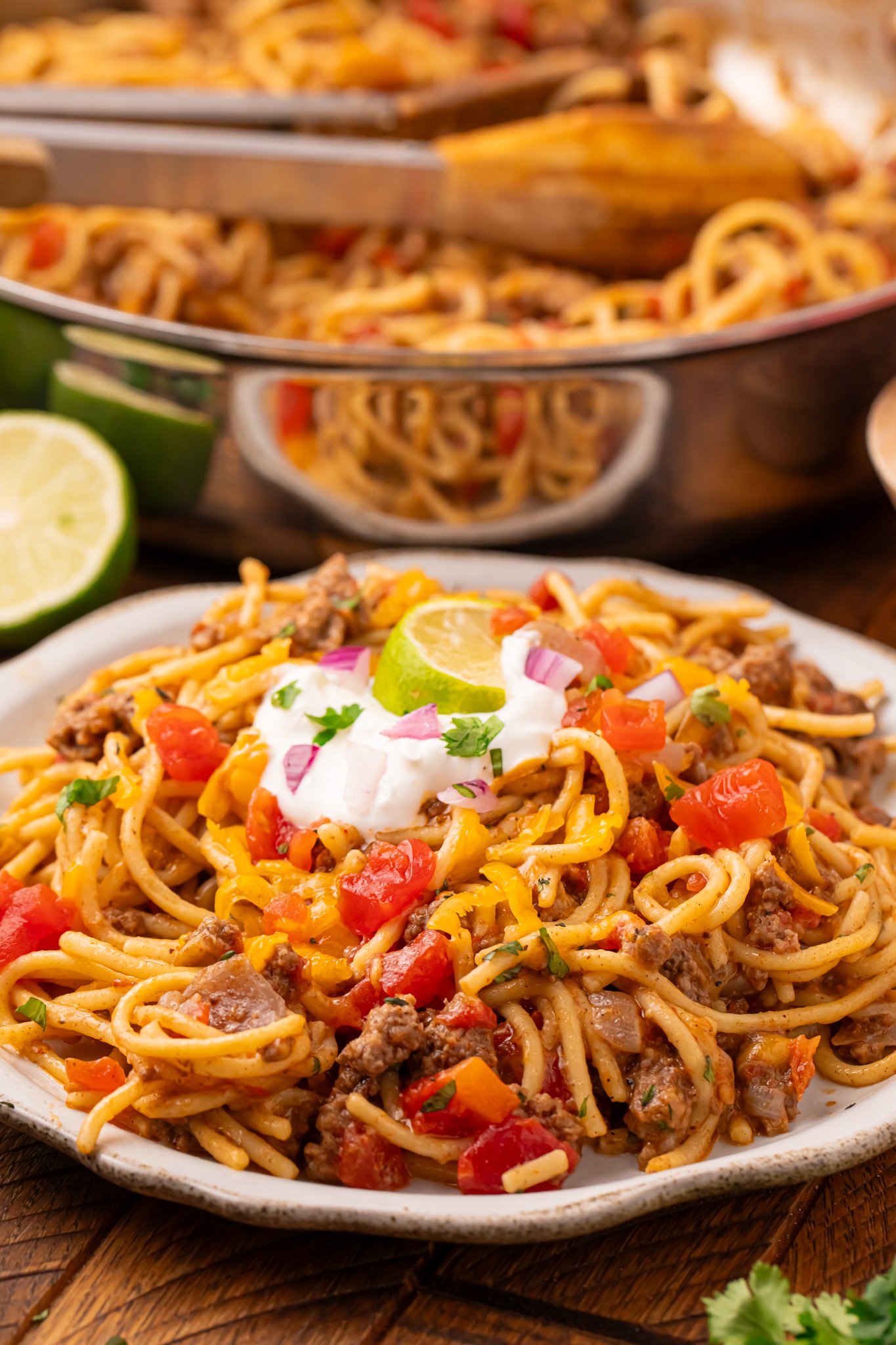 Cheesy Taco Spaghetti on a white plate sitting on a dark wood table 