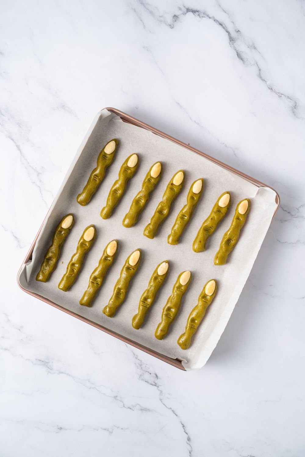 raw pistachio Witch Finger Cookies on a parchment paper lined tray with almonds for finger nails