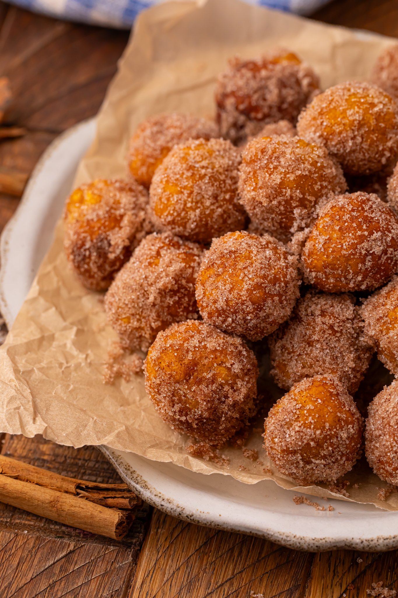 Up close shot of a pile of Pumpkin Pie Donut Holes stacked on a parchment lined white platter on a wooden table.