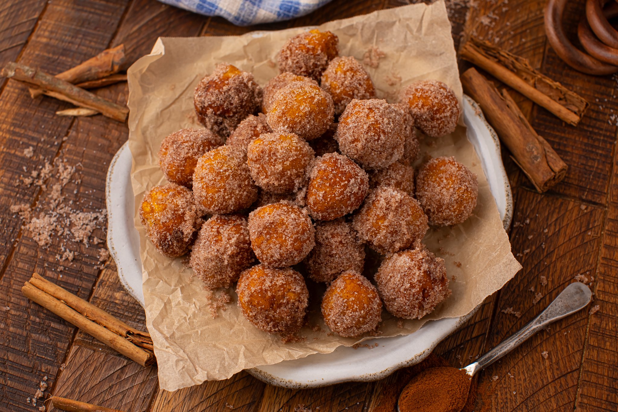 overhead shot of the Pumpkin Pie Donut Holes scattered on a parchment lined white platter on a dark wooden table. 
