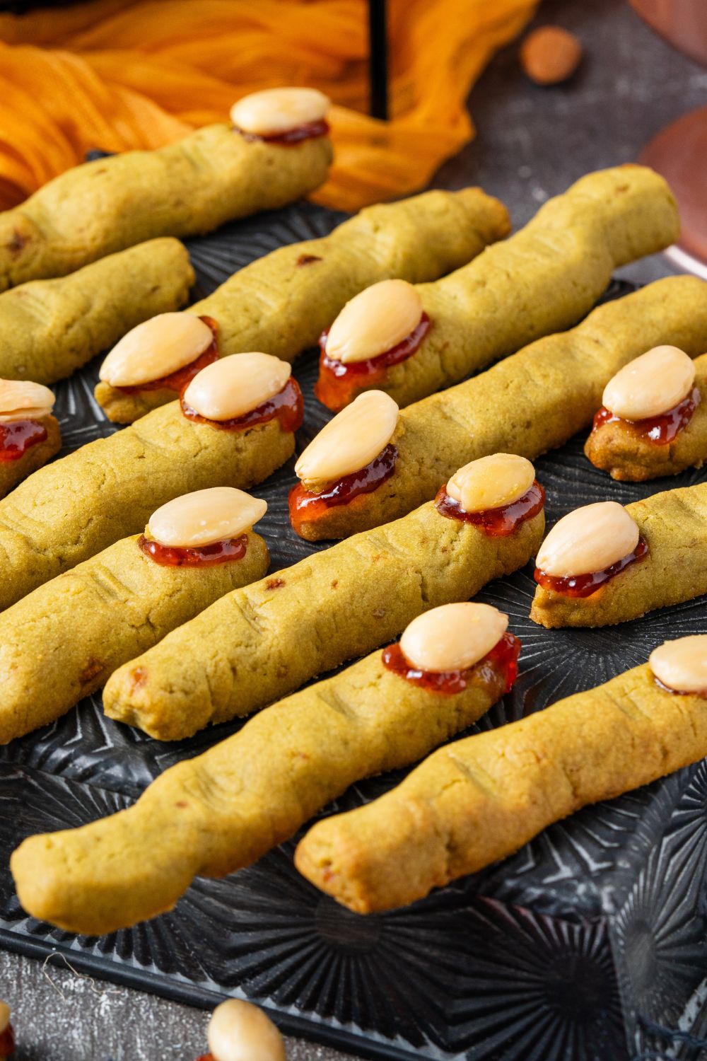 Witch Finger Cookies on a black tray on table with an orange towel behind it on the grey table 