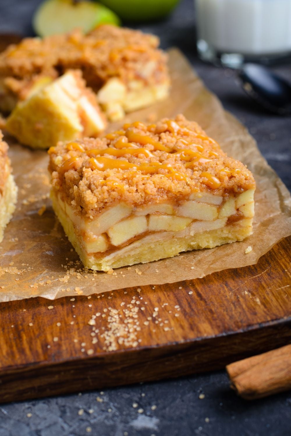 Caramel Apple Pie Bar on  wooden cutting board showing the layers of apples with a cinnamon stick in front