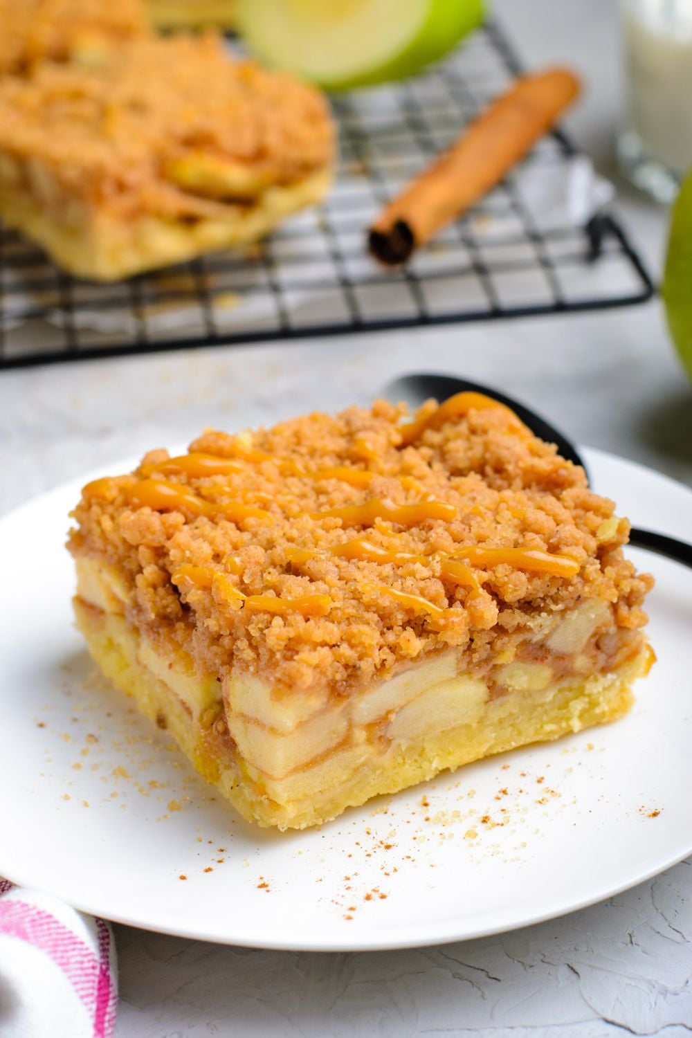 Caramel Apple Pie Bar on a plate with a spoon behind it on a white table 