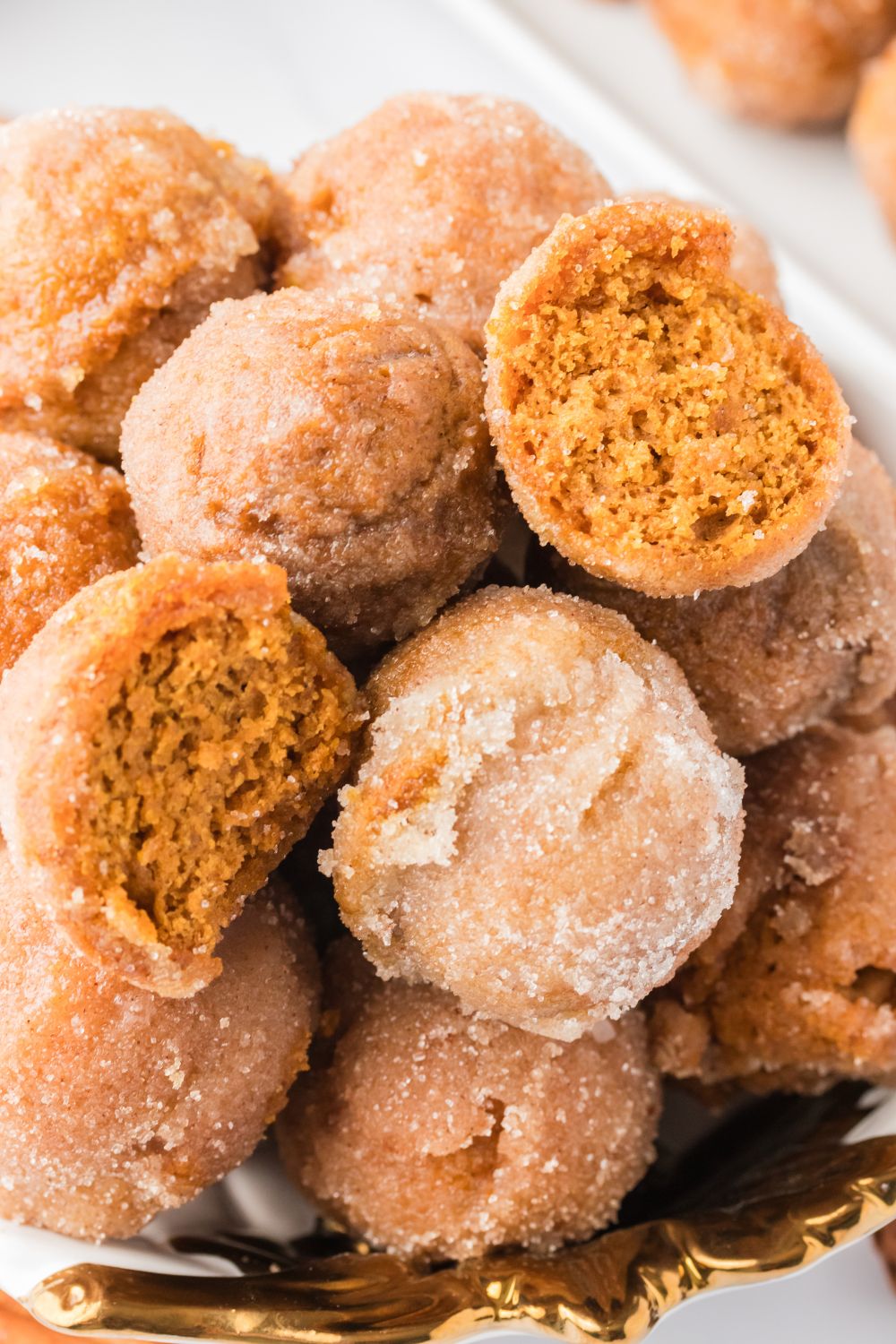 Pumpkin Spice Donut Holes stacked on a platter with one cut in half to see the fluffy center of the donut holes 