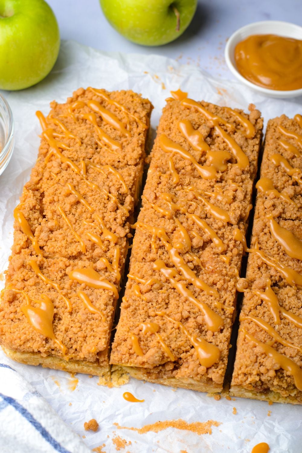 Caramel Apple Pie Bars cut into squares with a drizzle of caramel sauce on top sitting on a table 