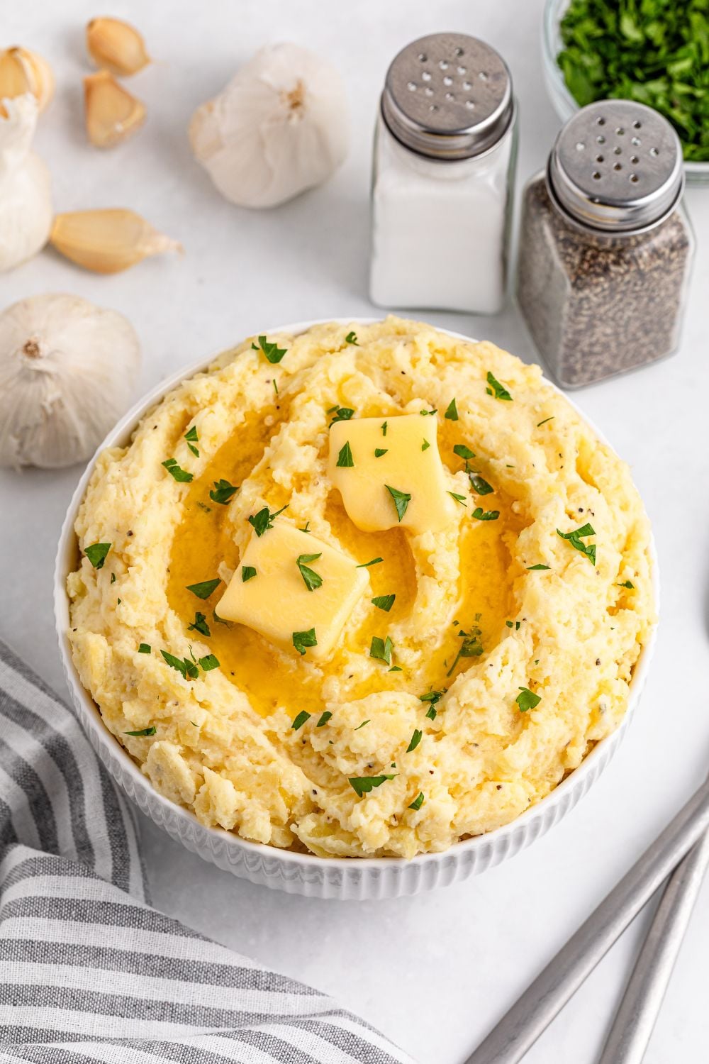 Garlic Mashed Potatoes placed in a white bowl with slabs of butter on top and some parsley