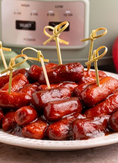 Crockpot Apple Butter BBQ Little Smokies on a white plate with toothpicks in it, with a slow cooker behind it on the table