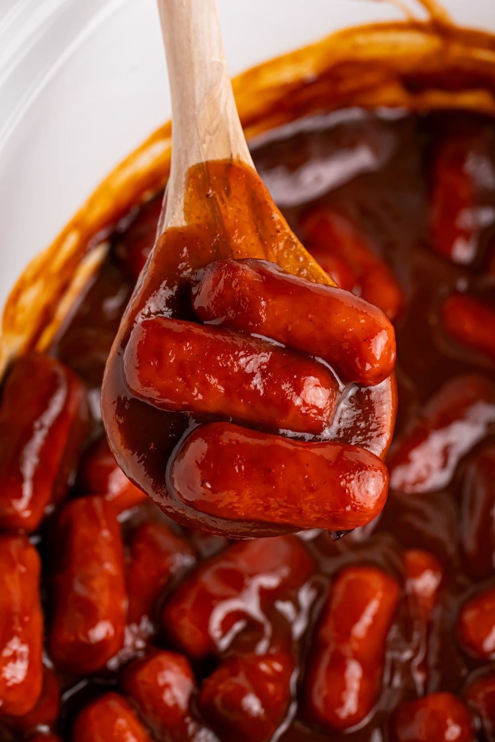 Crockpot full of little smokies with apple butter and a wooden spoon scooping some of the lil smokies out of the crockpot