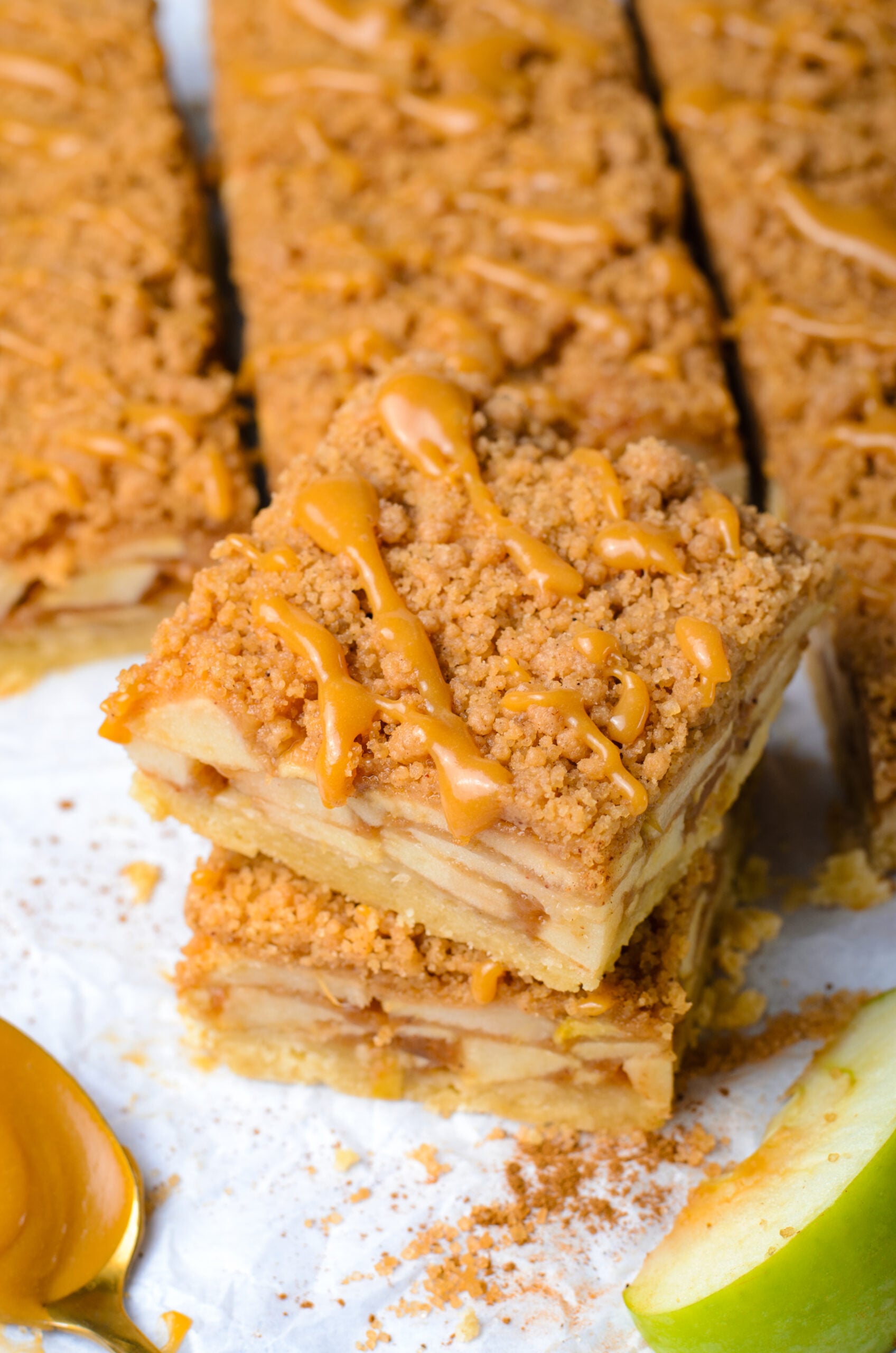Caramel Apple Pie Bars stacked then  placed on parchment paper showing apples in the center of the bars 