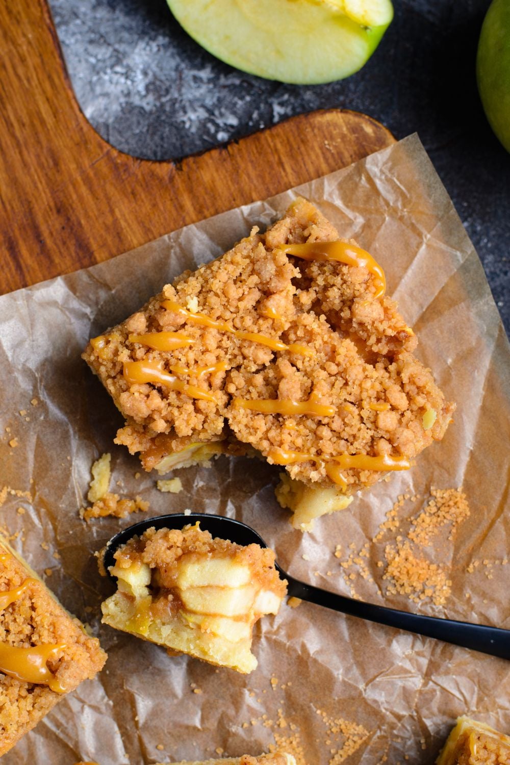 Caramel Apple Pie Bar on parchment table on a wooden table with a bite cut out of it on spoon 