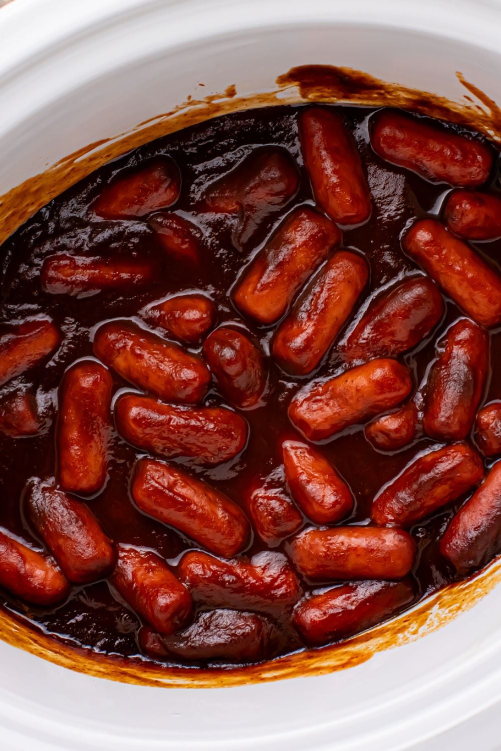 overhead look of a white crockpot full of bbq sauce smokies  