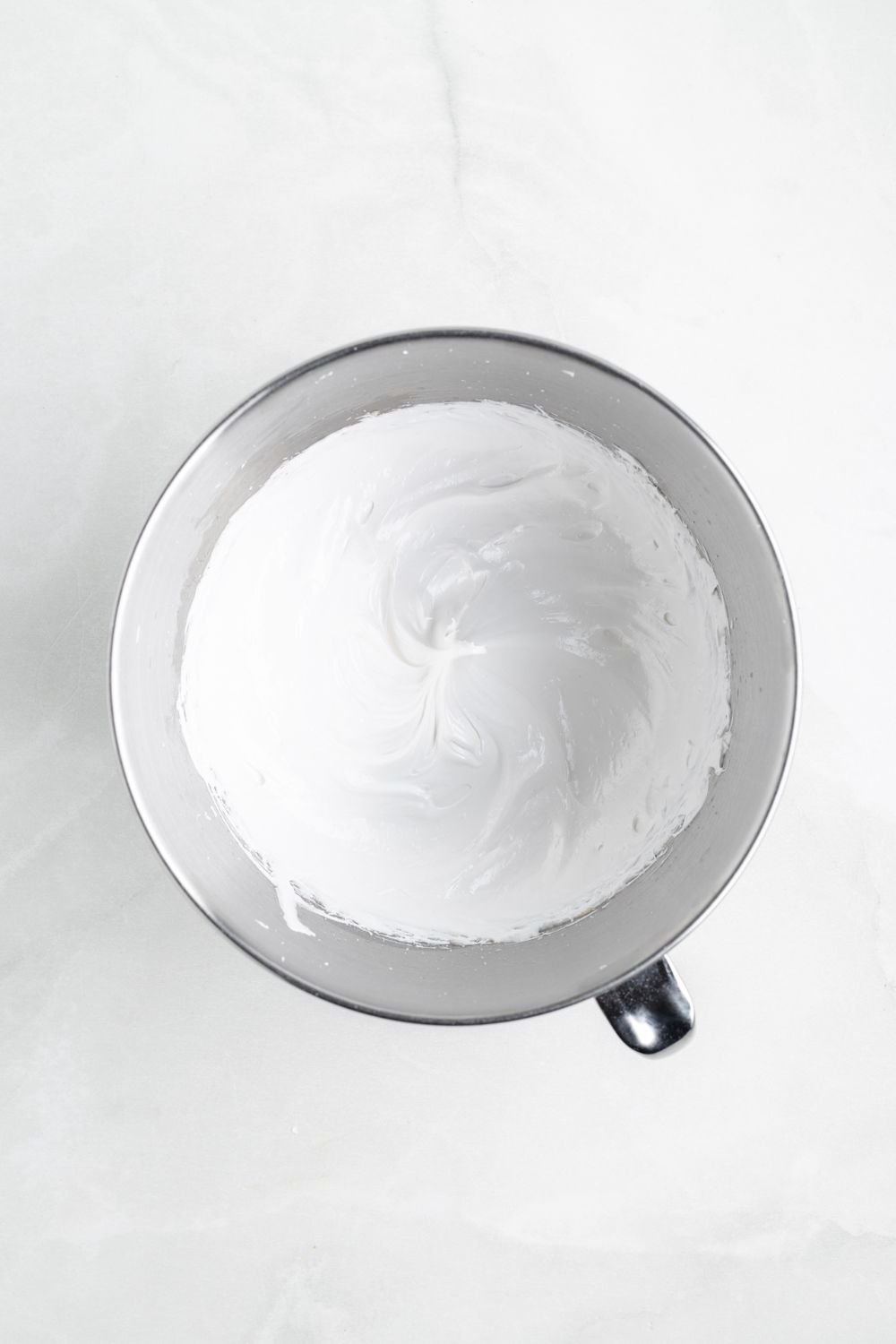 fluffy whipped meringue in a metal mixing bowl on a white counter