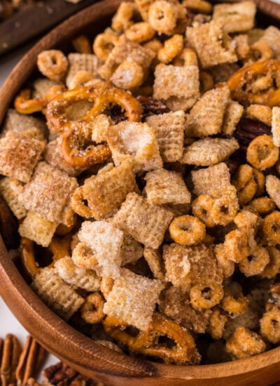 Pumpkin Spice Chex Mix in a wooden bowl on table with more mix scattered on table with a towel to the side of the bowl