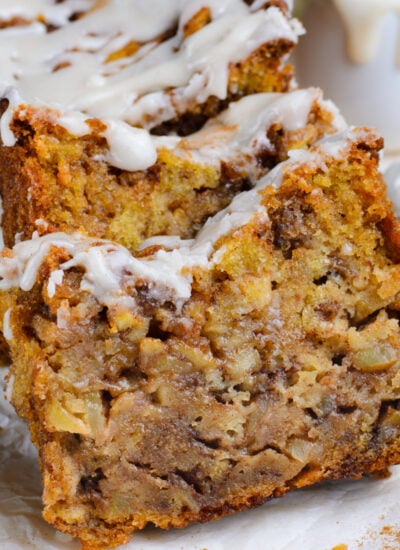 Amish Apple Fritter Bread sliced and placed on a parchment paper on table with a bowl with glaze to the side