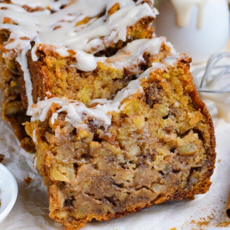 Amish Apple Fritter Bread sliced and placed on a parchment paper on table with a bowl with glaze to the side