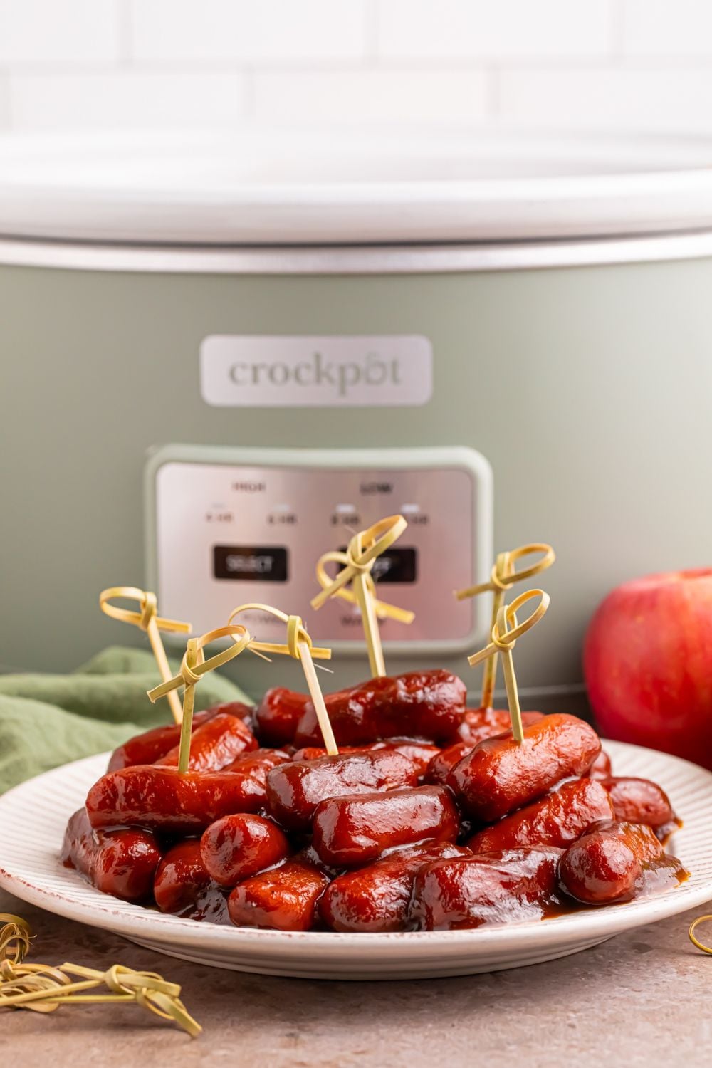 crockpot on the table and in front of it you have a white plate full of bbq smokies with toothpicks for serving as an appetizer 
