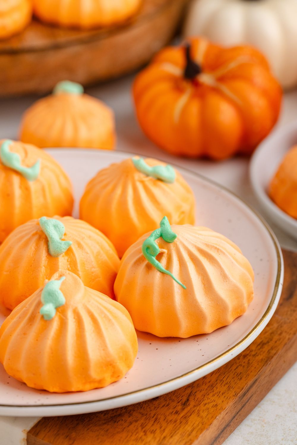 Pumpkin Meringue cookies on a plate with faux pumpkins behind it on table and a tray with more cookies 