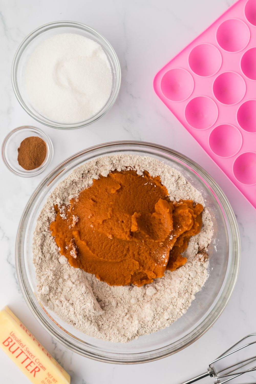dry ingredients and pumpkin puree in a glass bowl on a marble counter 