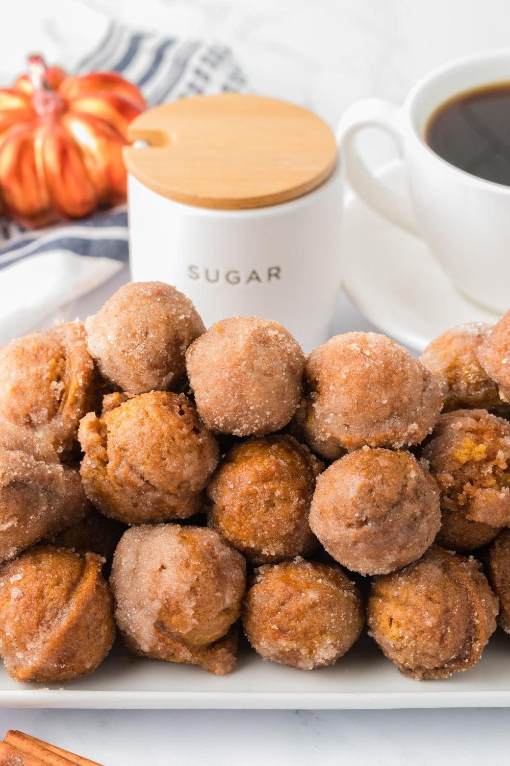 white rectangle chair on table stacked with pumpkin donut holes, and a cup of coffee and fall decor behind it on the table 