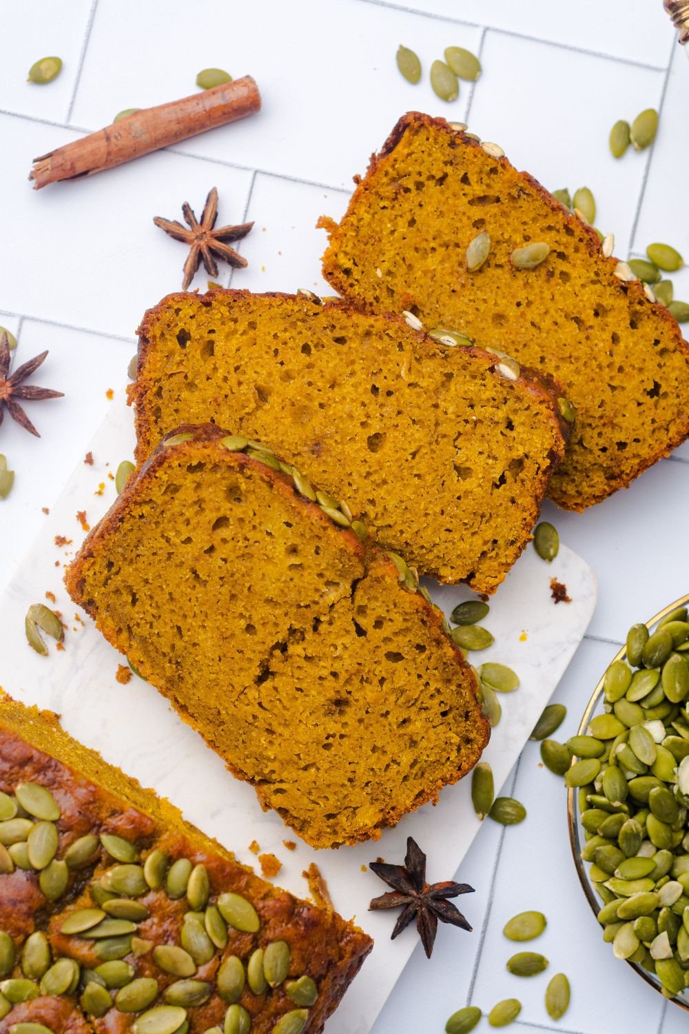 slices of Starbucks Pumpkin Bread placed on table and the rest of the remaining loaf setting on a white table with pumpkin seeds in a glass bowl to the side 