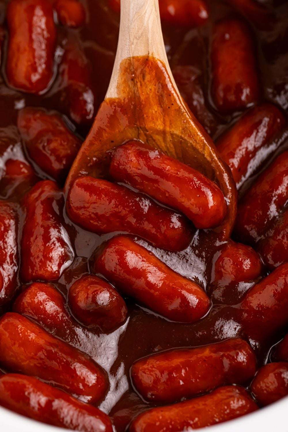 looking down on a slow cooker full of lil smokies in an apple butter and bbq sauce mixture with a wooden spoon scooping some up