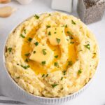 Garlic Mashed Potatoes in a white bowl sitting on a white table with salt and pepper shaker to the side of table