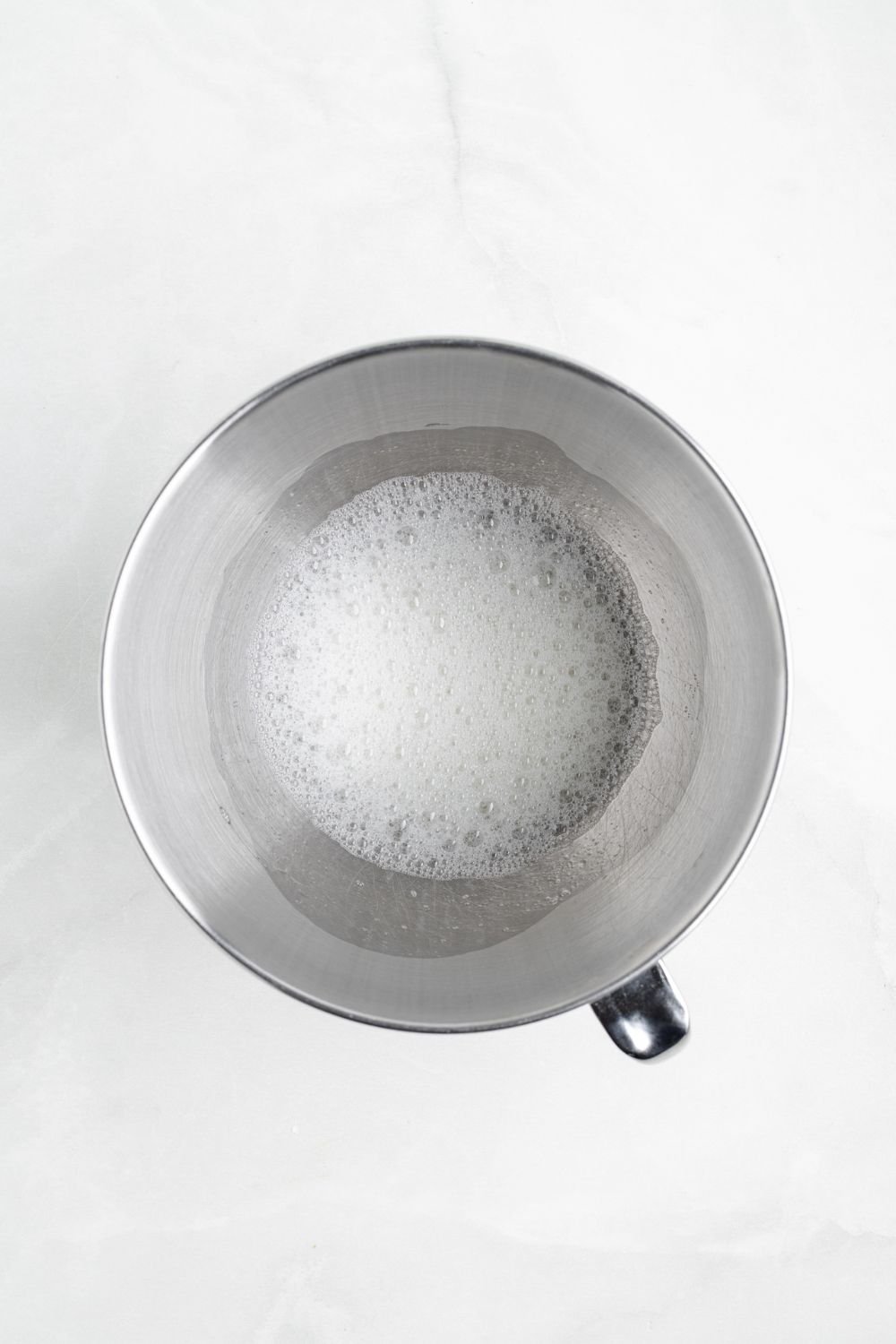 egg whites in a metal mixing bowl on a white counter 