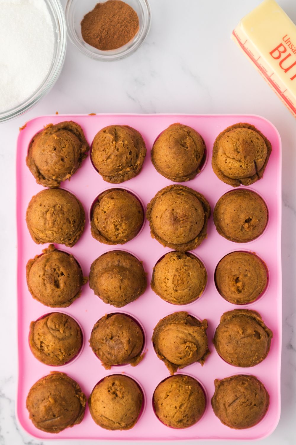 baked Pumpkin Spice Donut Holes in a pink pan sitting on a marble counter