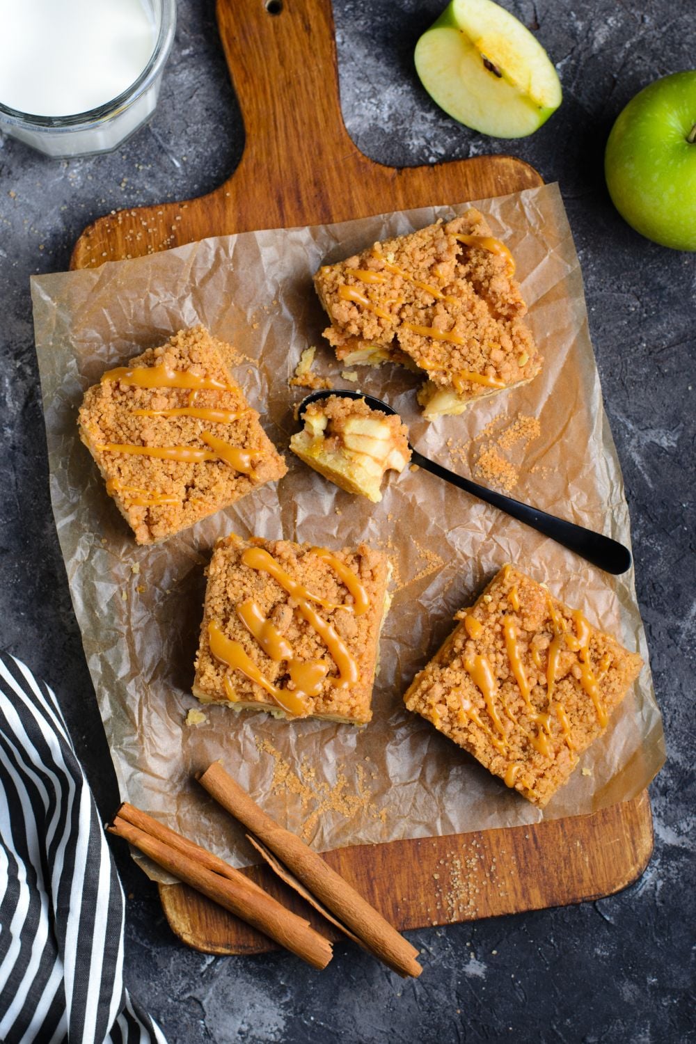 wooden cutting board with slices of apple bars on table with apples around table