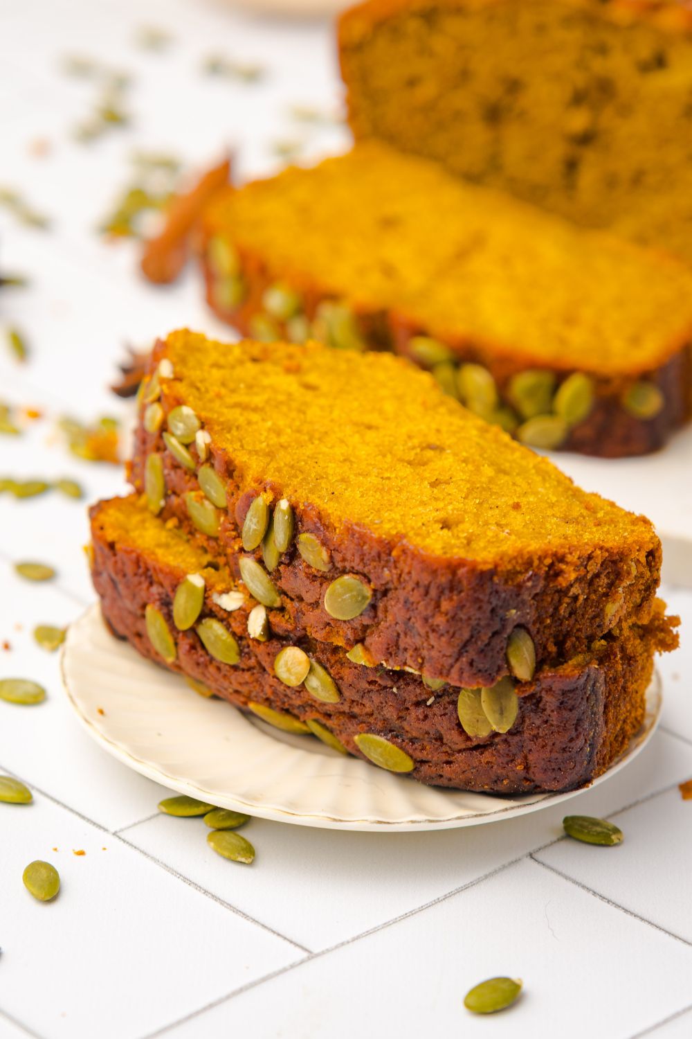 slices of Starbucks Pumpkin Bread on a white plate with more bread behind it on the white table and seeds scattered around the table 