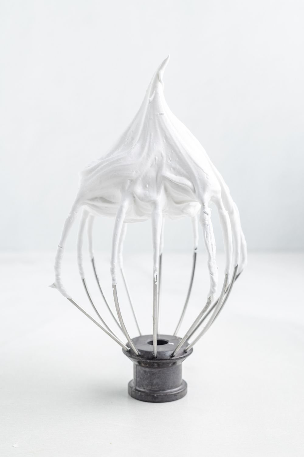 a whisk sitting on table with stiff meringue on it 