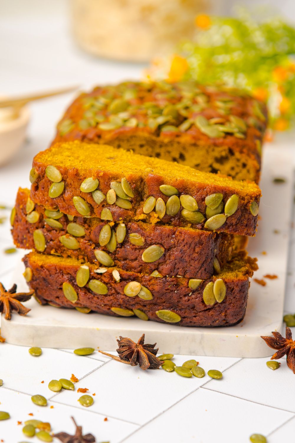 three slices of Starbucks Pumpkin Bread stacked on top of one another, with the rest of the pumpkin loaf behind it on a white table 