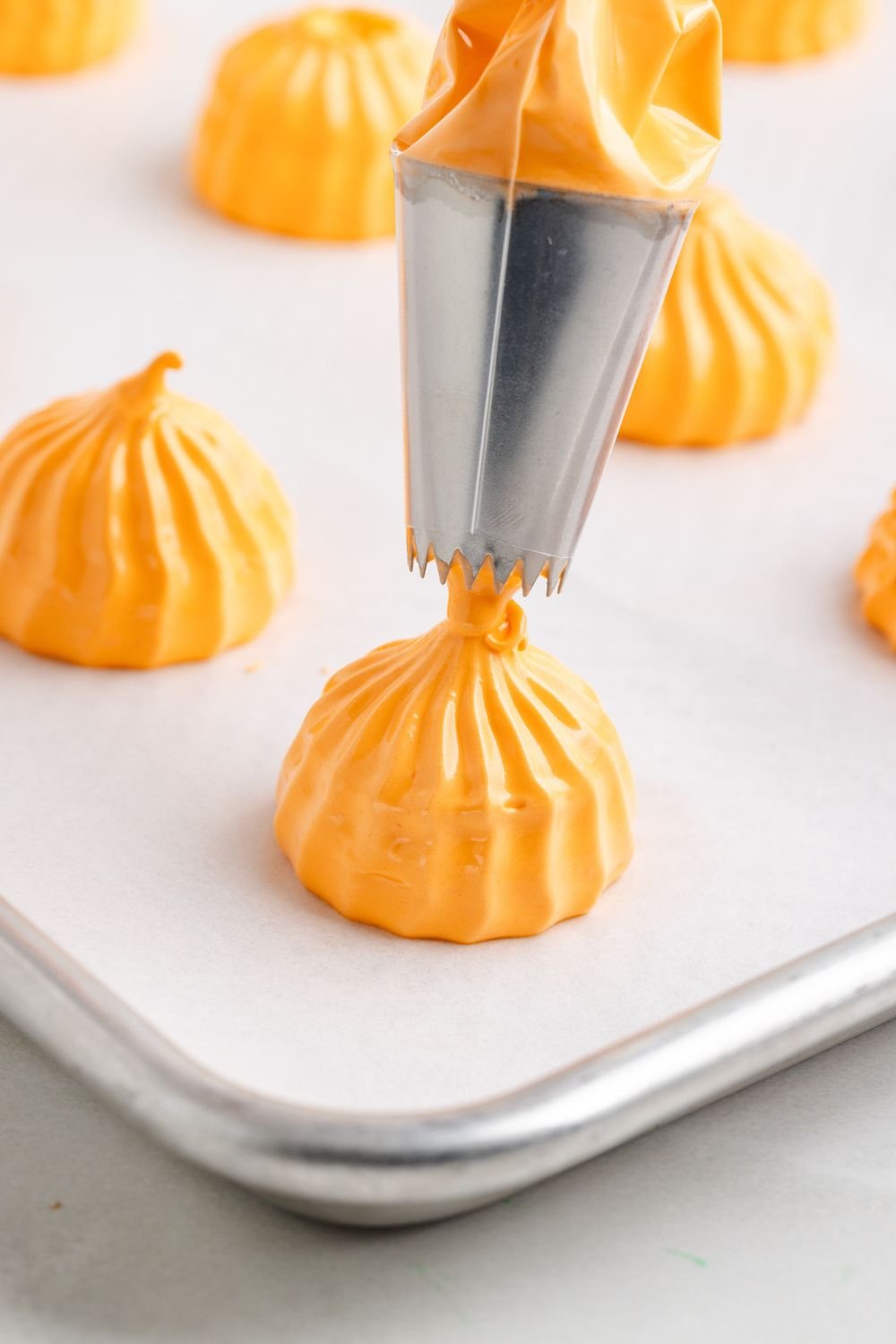 piping out a Pumpkin Meringue cookie shape onto a metal baking sheet with parchment paper 