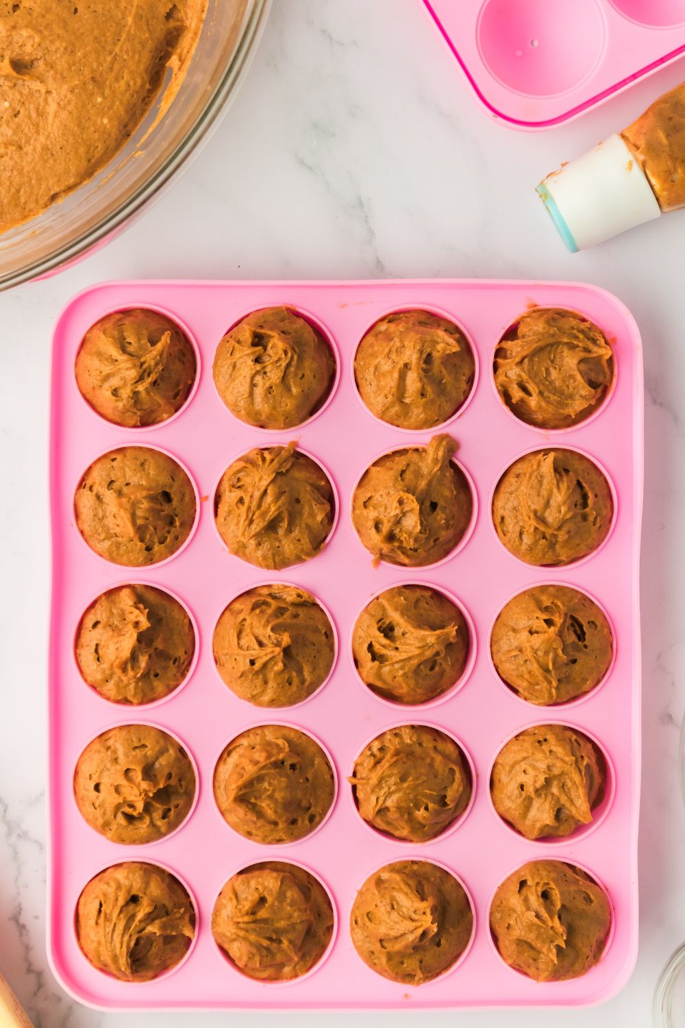 raw batter for Pumpkin Spice Donut Holes in a pink donut pan sitting on a marble counter 